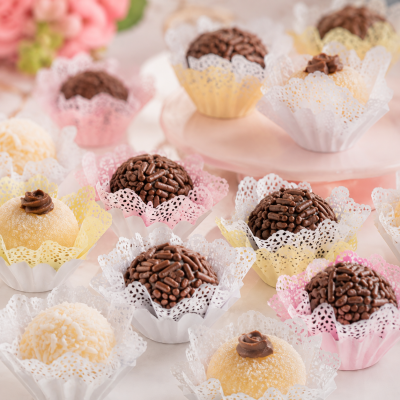 Brigadeiros e beijinhos em forminhas coloridas sobre superfície clara.