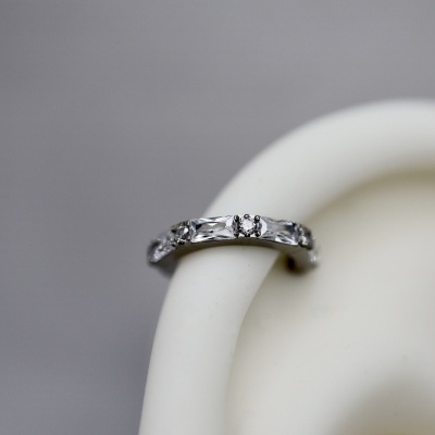 Anel prateado com pedras brilhantes numa superfície branca curva