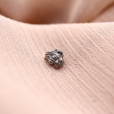 Pendente prateado em forma de abelha sobre tecido cor de rosa claro