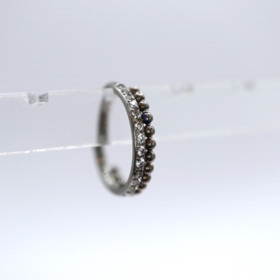 Anel prateado com pedras pretas e claras em suporte transparente