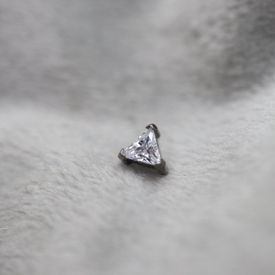 Pedra preciosa triangular transparente em engaste metálico sobre tecido cinzento