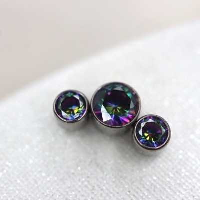 Três joias redondas com pedras iridescentes em molduras prateadas sobre superfície branca