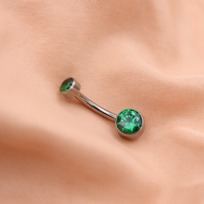 Piercing para umbigo com pedras verdes sobre tecido cor de pêssego