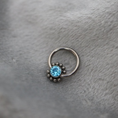 Anel de aço prateado com pedra azul sobre tecido cinzento