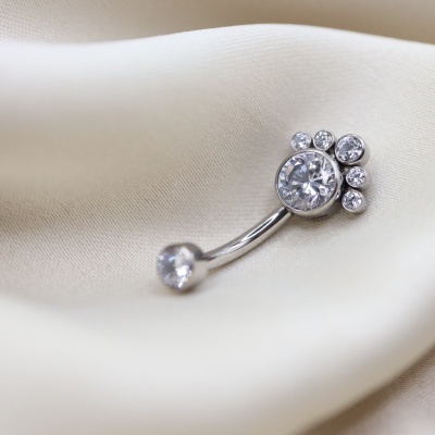 Piercing de umbigo prateado com pedras brilhantes sobre tecido bege
