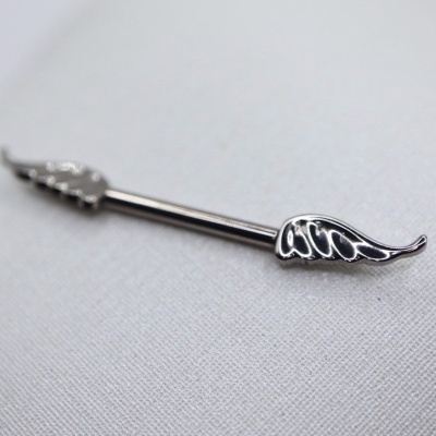 Alfinete metálico prateado com asas sobre tecido branco
