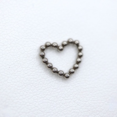 Colar em forma de coração feito de esferas metálicas prateadas numa superfície branca texturizada