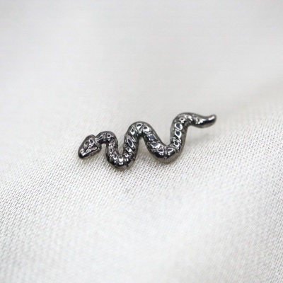Broche metálico em forma de serpente sobre tecido branco
