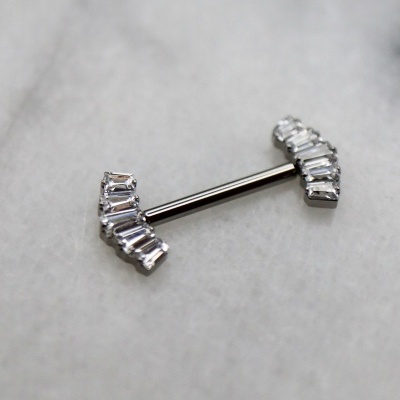 Piercing de barra em metal prateado com pedras retangulares transparentes sobre fundo cinza