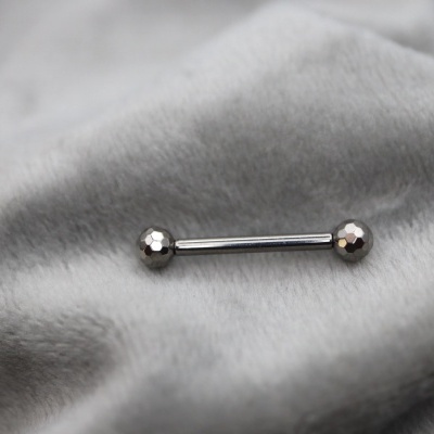 Barra de piercing metálica prateada sobre tecido cinza