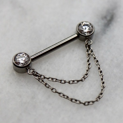 Brinco ou piercing prateado com pedras e correntes sobre mármore branco