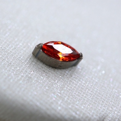 Gema vermelha oval com suporte metálico sobre tecido branco