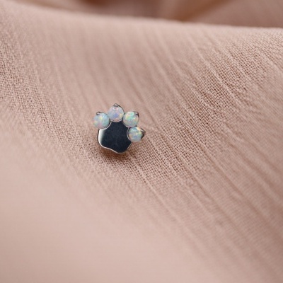 Brinco em forma de pata com pedras translúcidas sobre tecido rosa claro