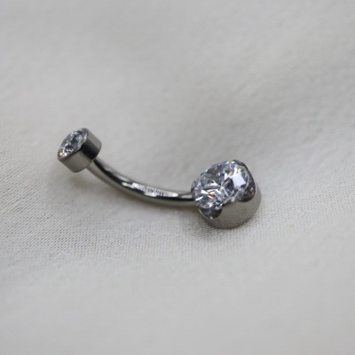 piercing de umbigo em metal prateado com pedras brilhantes sobre tecido bege