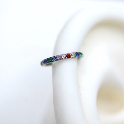 Argola prateada com pedras coloridas numa orelha de suporte branco