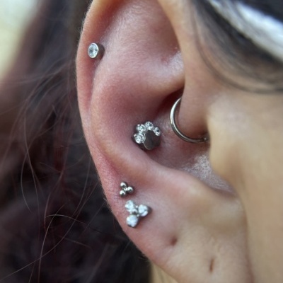 Orelha com vários piercings de metal prateado, alguns com pedras brilhantes.