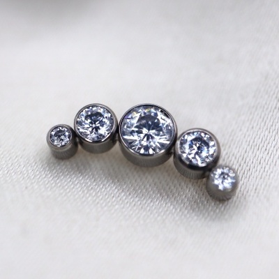 Brincos ou piercing de metal prateado com cinco pedras transparentes sobre tecido branco