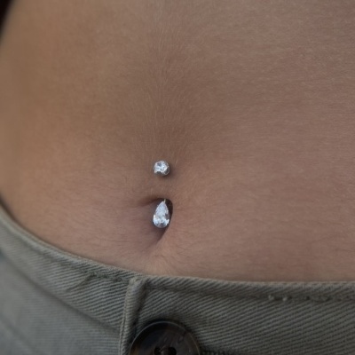 Piercing de umbigo com pedras brilhantes em pele com calças verdes