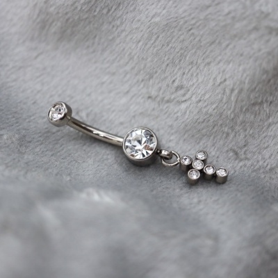 Piercing prateado com pedras transparentes e cruz pendente sobre tecido cinzento