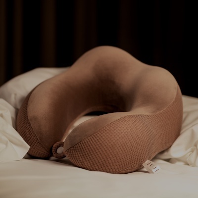 Almofada de pescoço castanha em forma de U sobre lençol branco