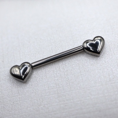 Barra de piercing prateada com pontas em forma de corações sobre tecido branco