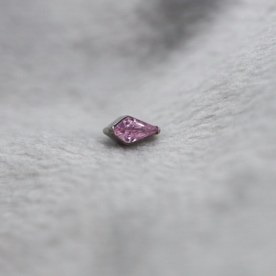 Pedra preciosa rosa em forma de gota sobre superfície cinzenta