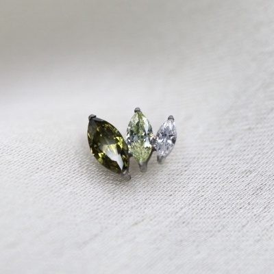 Três pedras preciosas cortadas em marquesa, verde-oliva, verde-clara e incolor, sobre tecido branco.