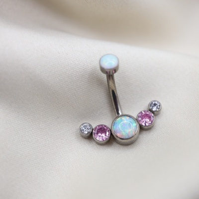 Brinco de umbigo prateado com pedras opalas e rosas sobre tecido bege