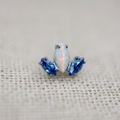 Brincos pequenos com pedras opalescentes e azuis sobre tecido bege