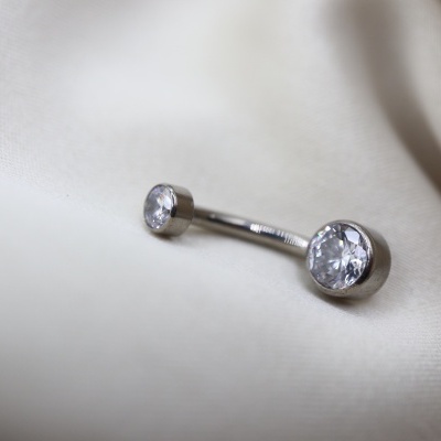 Piercing para umbigo em aço inoxidável com pedras transparentes sobre tecido creme