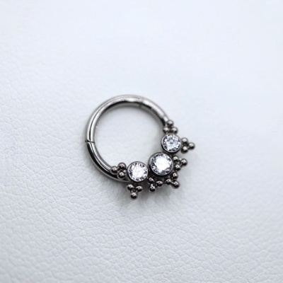 Anel de argola prateada com pedras e detalhes esféricos em superfície branca