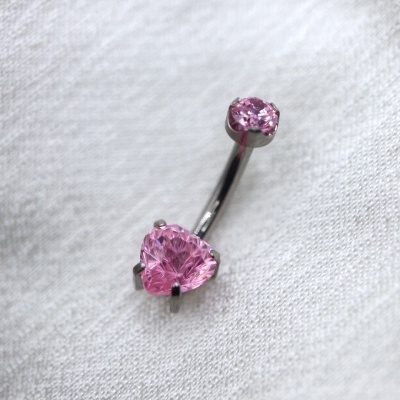Piercing umbigo em metal prateado com pedras cor-de-rosa sobre tecido branco