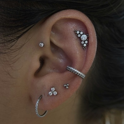 Orelha com vários brincos prateados com pedras brilhantes