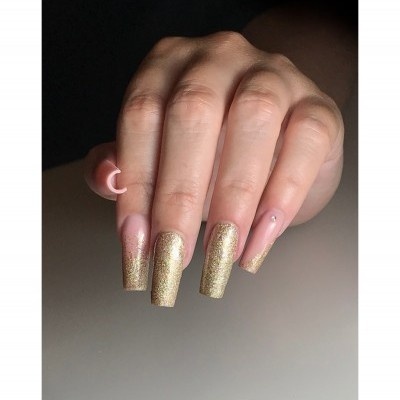 Mão feminina com unhas decoradas em dourado glitter e base nude com strass.