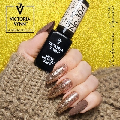Mão com unhas decoradas em castanho mate e glitter dourado segurando verniz gel Victoria Vynn