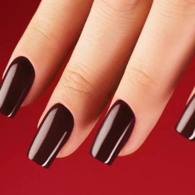 Unhas com verniz vinho escuro e brilho sobre fundo vermelho.