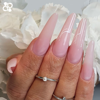 Mãos com unhas compridas rosa e desenhos brancos, anéis prateados e flores brancas ao fundo