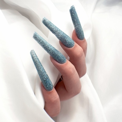 Unhas compridas azuis com glitter sobre tecido branco