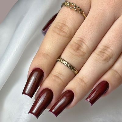 Mão com unhas compridas e verniz bordeaux e dois anéis dourados