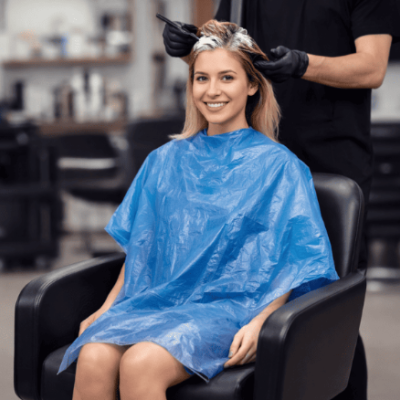 Mulher no salão de cabeleireiro com capa azul e cabeleireiro aplicando produto no cabelo.