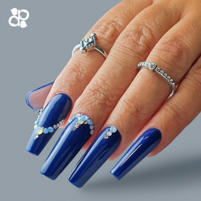 Mãos femininas com unhas azuis decoradas com cristais e anéis prateados