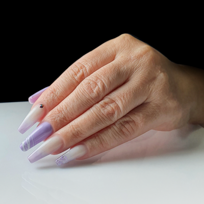 Mão com unhas compridas decoradas em lilás e nude com desenhos geométricos.