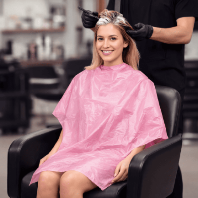 Mulher sentada com capa rosa a preparar cabelo para coloração