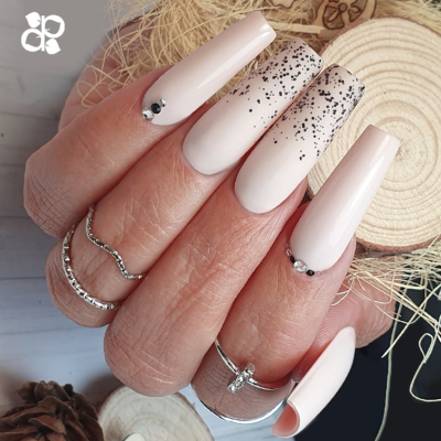 Unhas compridas nude com pedras brilhantes e manchas pretas, fundo de madeira e palha