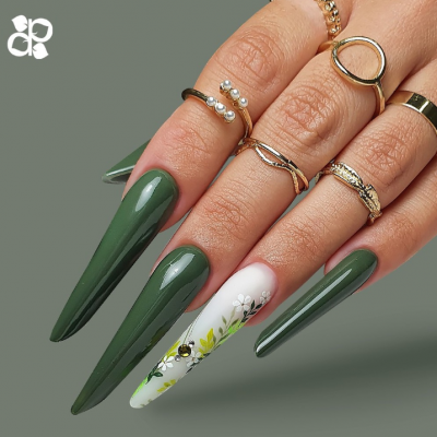 Unhas estileto verdes com uma unha decorada com flores brancas e folhas, com anéis dourados