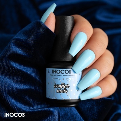 Frasco de verniz para unhas INOCOS azul claro e mão com unhas azuis longas