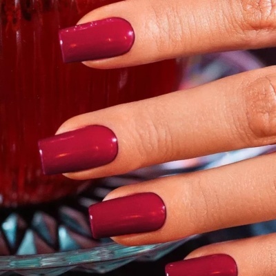 Mãos com unhas bordô brilhantes e quadradas.