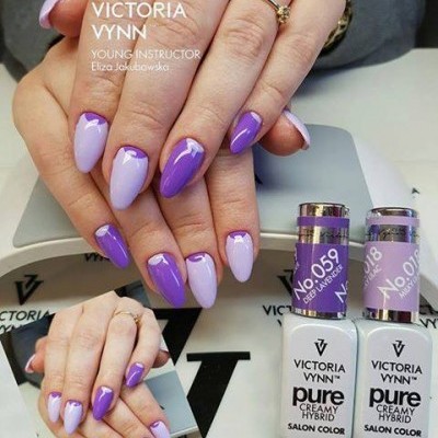 Unhas pintadas em roxo e lilás com design em V, frascos de verniz Victoria Vynn sobre mesa branca.