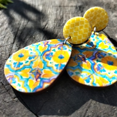 Brincos coloridos em forma de gota com base redonda amarela sobre madeira