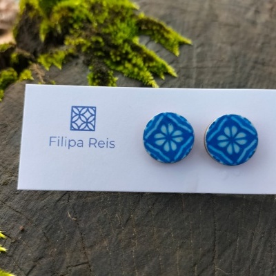 Brincos azuis redondos com padrão branco em cartão branco, sobre madeira e musgo verde